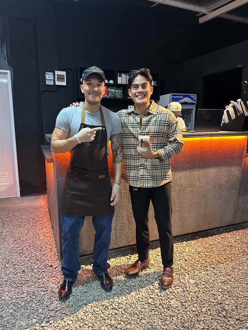 Enver at the Ruje Café counter with a drink, beside Russ