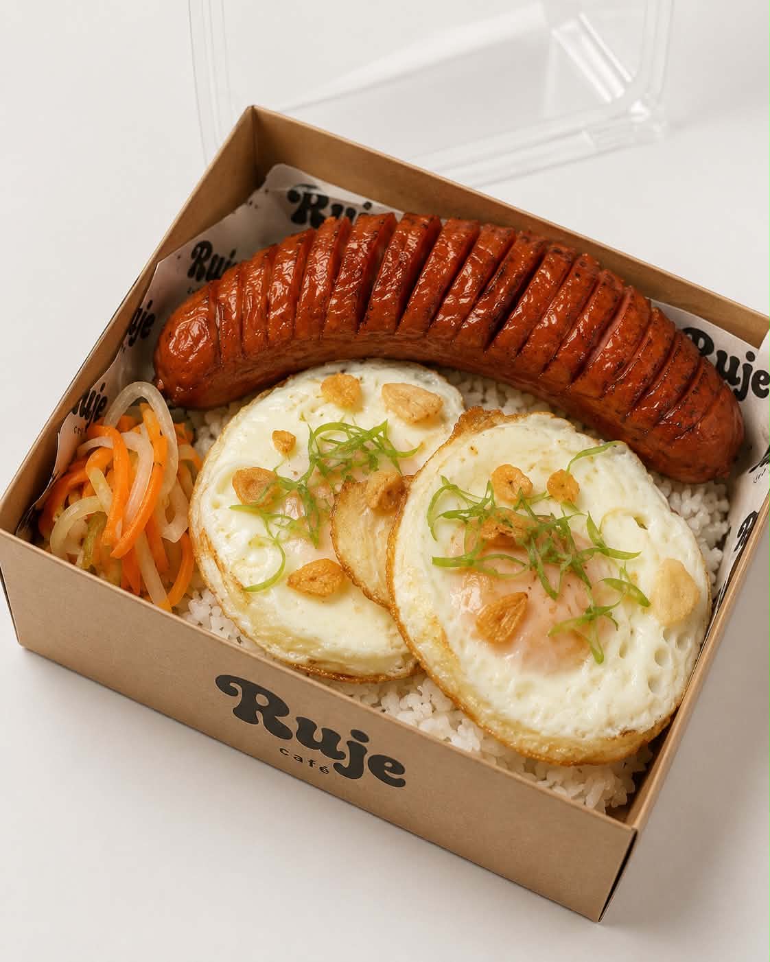 A Ruje Café rice meal box: grilled sausage, two garlic fried eggs, and pickled vegetables on rice